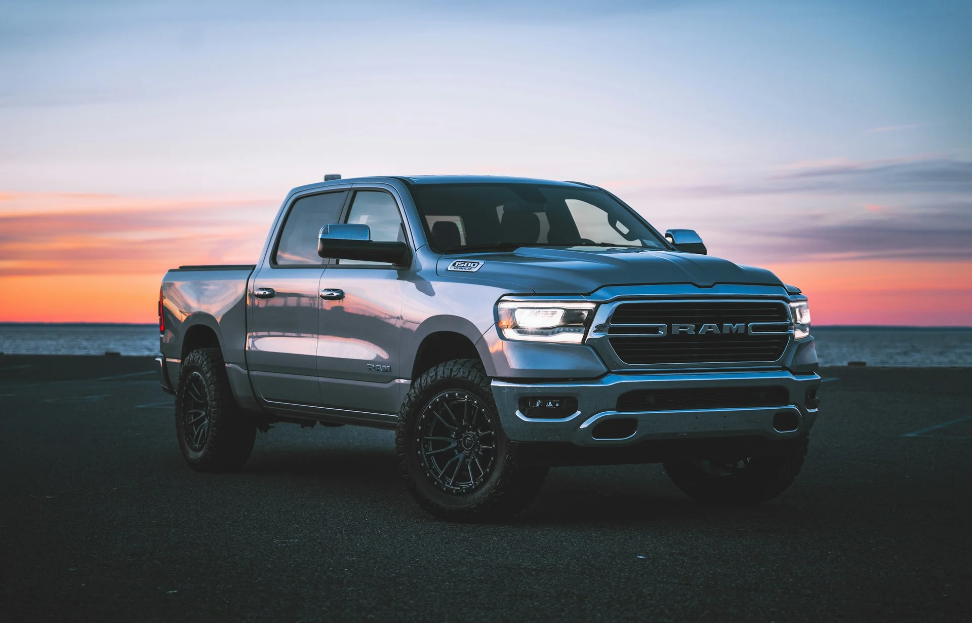 Silver Ram 1500 pickup parked beside the water at sunset.